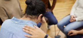 Personne réconfortée par une main posée sur son épaule, au sein d'un groupe de soutien après un traumatisme. 