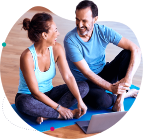 Un homme et une femme en tenue de sport, assis sur un tapis de yoga, souriant et discutant. 
