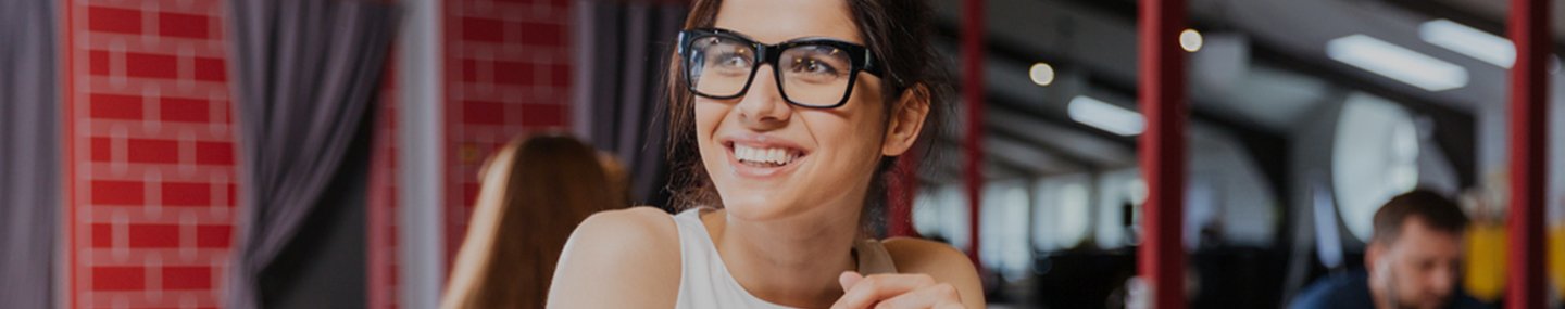 Jeune collaboratrice heureuse et souriante assise sur son lieu de travail, devant son ordinateur, avec des lunettes
